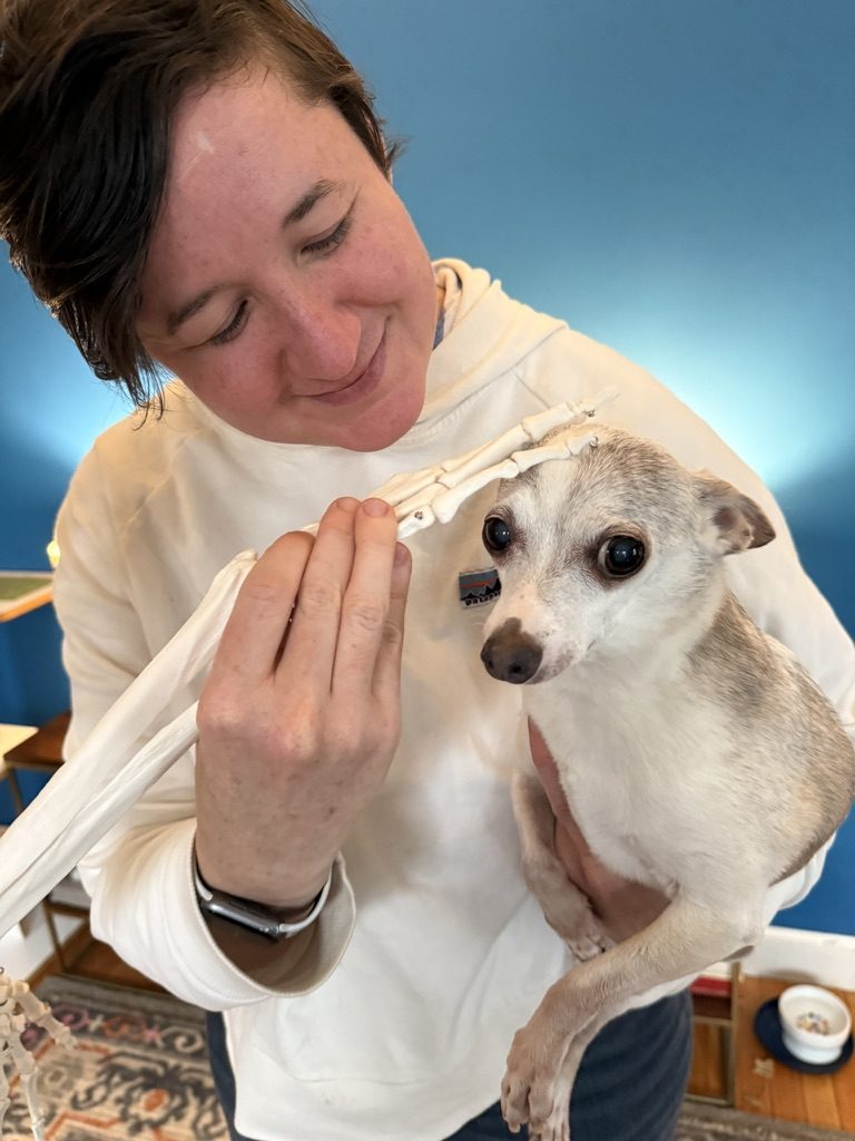 Virginia holding her senior dog, Thor, while touching a skeleton hand model to his head.
